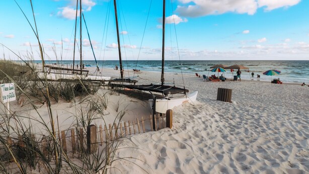 Una playa con una valla de madera, un bote y sombrillas.