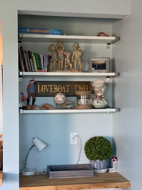 A shelf with books, figurines, a sign reading "LOVEBOAT TWO", a lamp, and a small plant.