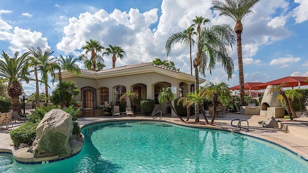 A pool area with a clear blue pool, palm trees, and a building with arched windows.