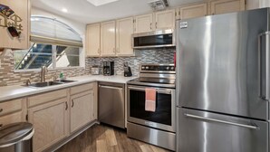A modern kitchen with stainless steel appliances, wooden cabinets, a dishwasher, and a window with a view.