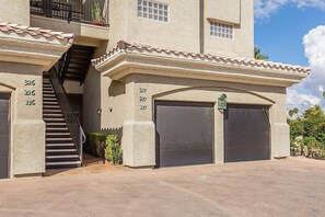 A two-story building with a stucco exterior, a tiled roof, and a set of stairs leading to the entrance. There are two garage doors and a small window on the upper floor.