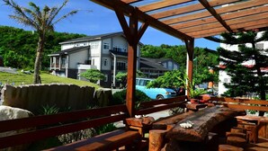 An outdoor wooden deck with benches and a large tree stump, overlooking a residential area with houses and a blue car. - Star-Moon B&B (Lyudao)