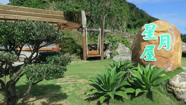 A stone sign with Japanese characters, a wooden swing, and a well-maintained garden with various plants. - Star-Moon B&B (Lyudao)