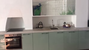 Una cocina moderna con horno empotrado, tetera, lavamanos y un espejo decorativo sobre la encimera.