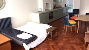 Una habitación de hotel compacta con una cama individual, una pequeña mesa de madera, una silla, una kitchenette y una ventana con vistas.
