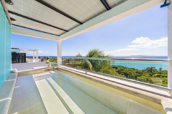 A balcony with a clear view of the ocean and greenery.
