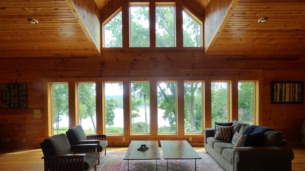 Un salón amplio con techo alto y ventanas grandes que ofrecen vistas a un lago y árboles.