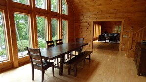 Interior de una cabaña de madera con una mesa de comedor, sillas y una zona de cocina.