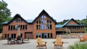 Un gran lodge de madera con una entrada principal destacada, varias ventanas y un porche cubierto con mobiliario exterior.
