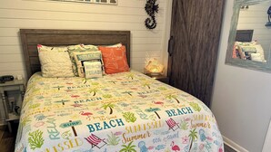 A bed with a beach-themed bedspread, a wooden headboard, and a bedside table with a lamp. - Stunning Oceanview Luxury Remodel, Bikes Included! (Hilton Head Island)
