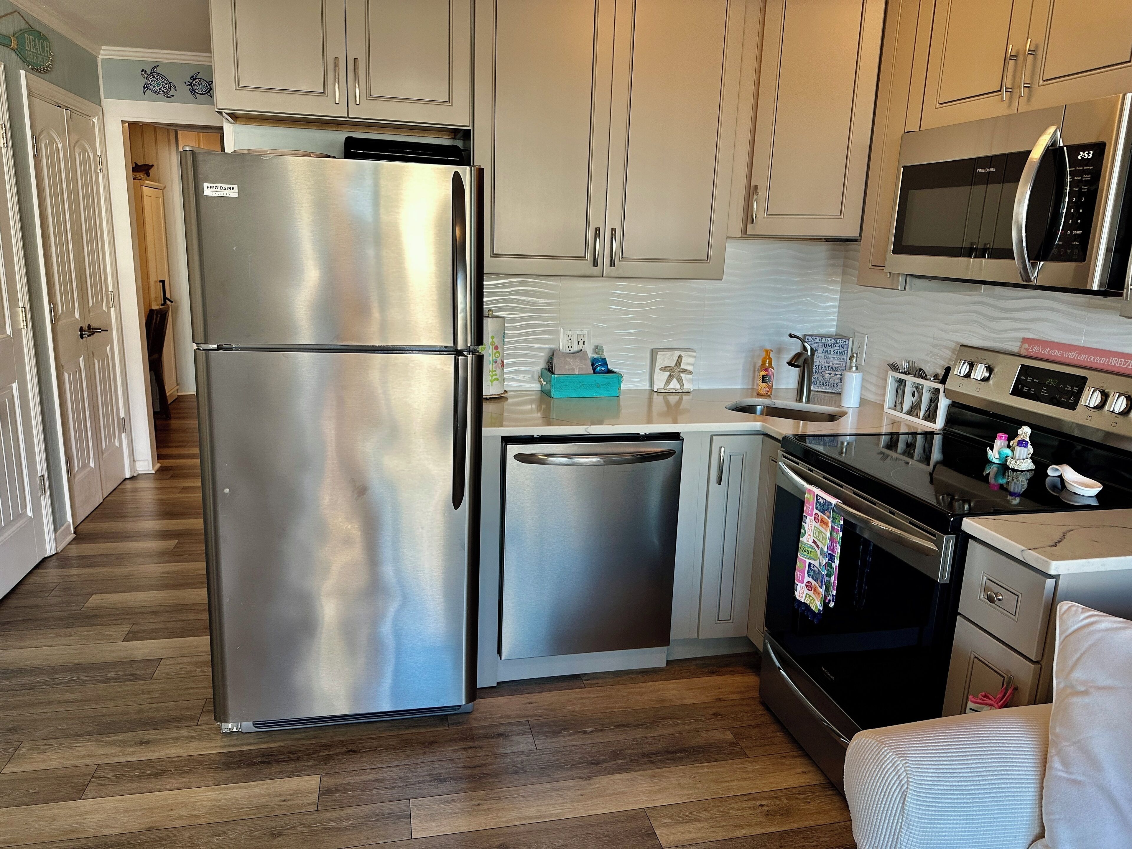 A modern kitchen with stainless steel appliances, wooden flooring, and light-colored cabinetry.