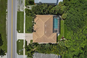 Vue aérienne d’une propriété comprenant un grand bâtiment à toit ouvert, une piscine et de nombreux espaces verts.