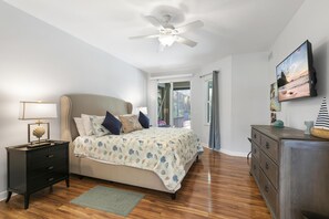 Une chambre à coucher comprenant un lit, une table de chevet, une commode, un ventilateur de plafond et une fenêtre donnant sur l’extérieur.