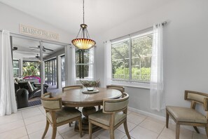 Un coin repas comprenant une table ronde, quatre chaises, un luminaire suspendu et une vue sur l’extérieur grâce à de grandes fenêtres.