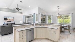 A modern kitchen with a corner island, built-in dishwasher, and a dining area with a round table and chairs. - 4Br Pristine Home Sleeps 6 Adu - Heated Pool + Spa - Private backyard (Marco Island)
