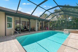 A covered swimming pool with a glass ceiling, lounge chairs, and a patio area.
