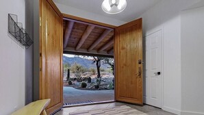Una habitación con un banco de madera, una puerta blanca y vista a un paisaje desértico a través de un vano abierto.