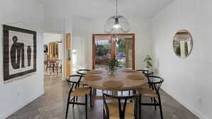 Un comedor con una mesa redonda, sillas negras, una lámpara colgante y un cuadro en la pared.