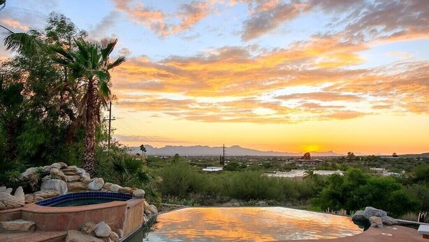 Zona de piscina con sillas de descanso, un jacuzzi y vistas al atardecer sobre un paisaje montañoso.