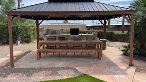 Un espacio al aire libre techado con zona de estar, una parrilla, suelo de piedra y una pérgola.