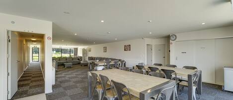 A spacious dining area with multiple tables and chairs, a staircase leading to another room, and a clock on the wall.