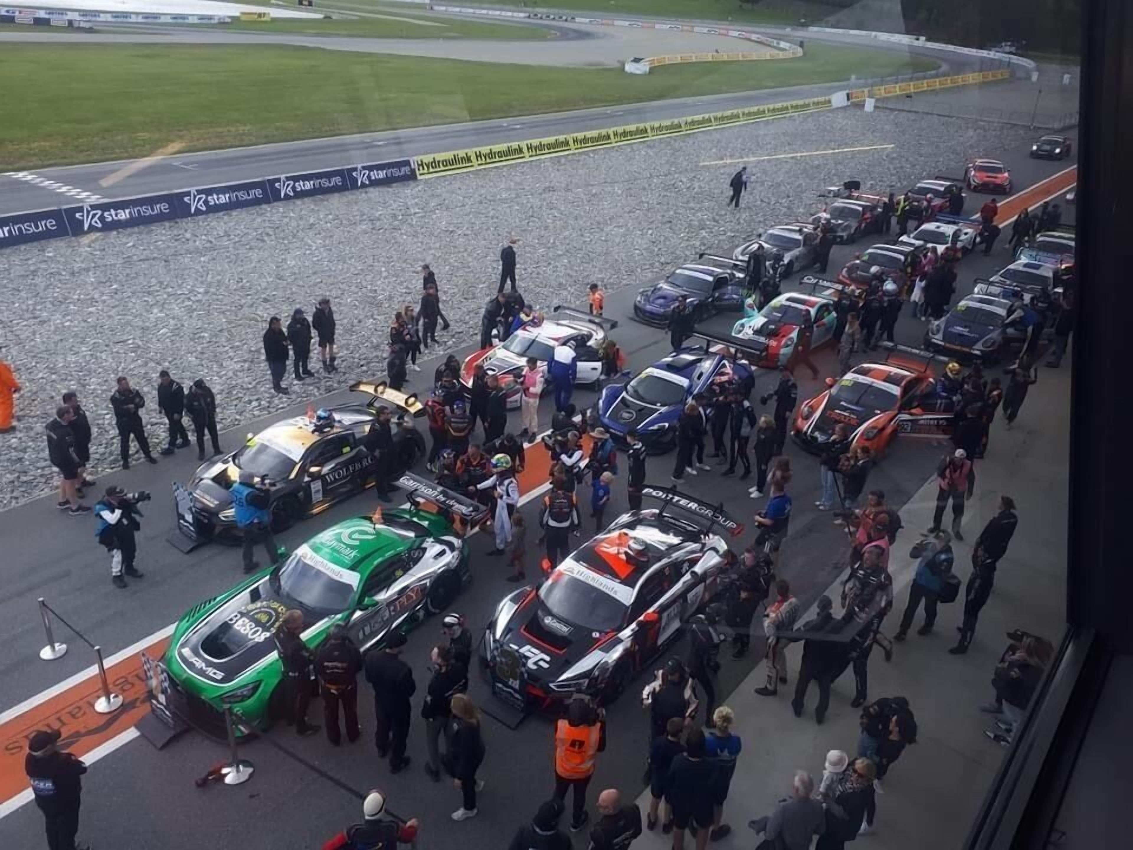 A parking area with multiple race cars and people gathered around.