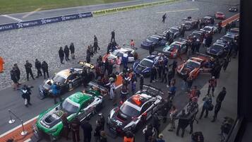 Un estacionamiento con varios coches de carreras y gente reunida.