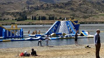 A water park with inflatable slides and play structures by a lake, surrounded by hills.