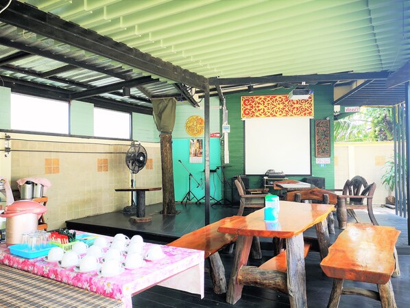 A restaurant with wooden tables and chairs, a stage with a microphone, and a fan.