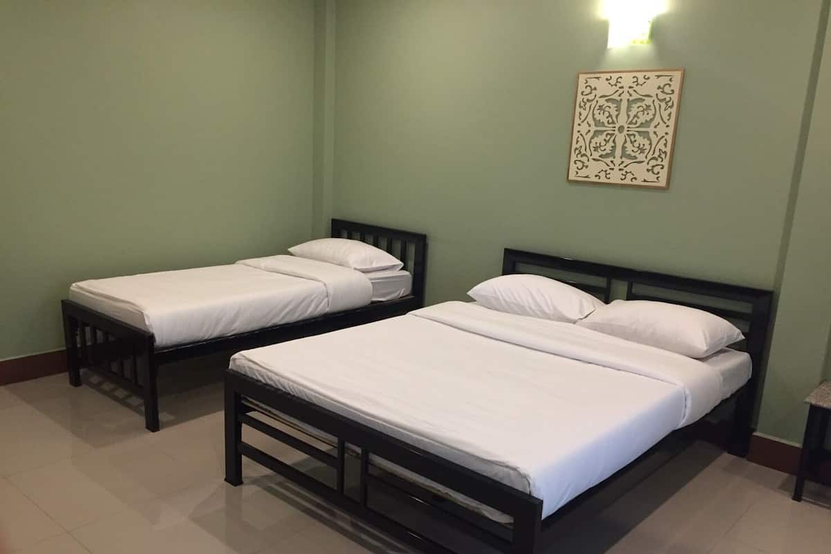 A room with two single beds and a larger bed, all with white bedding.