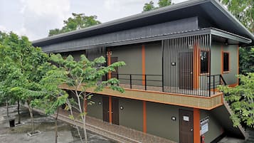 Stylish building with a flat roof and balcony, surrounded by lush greenery and a paved area.
