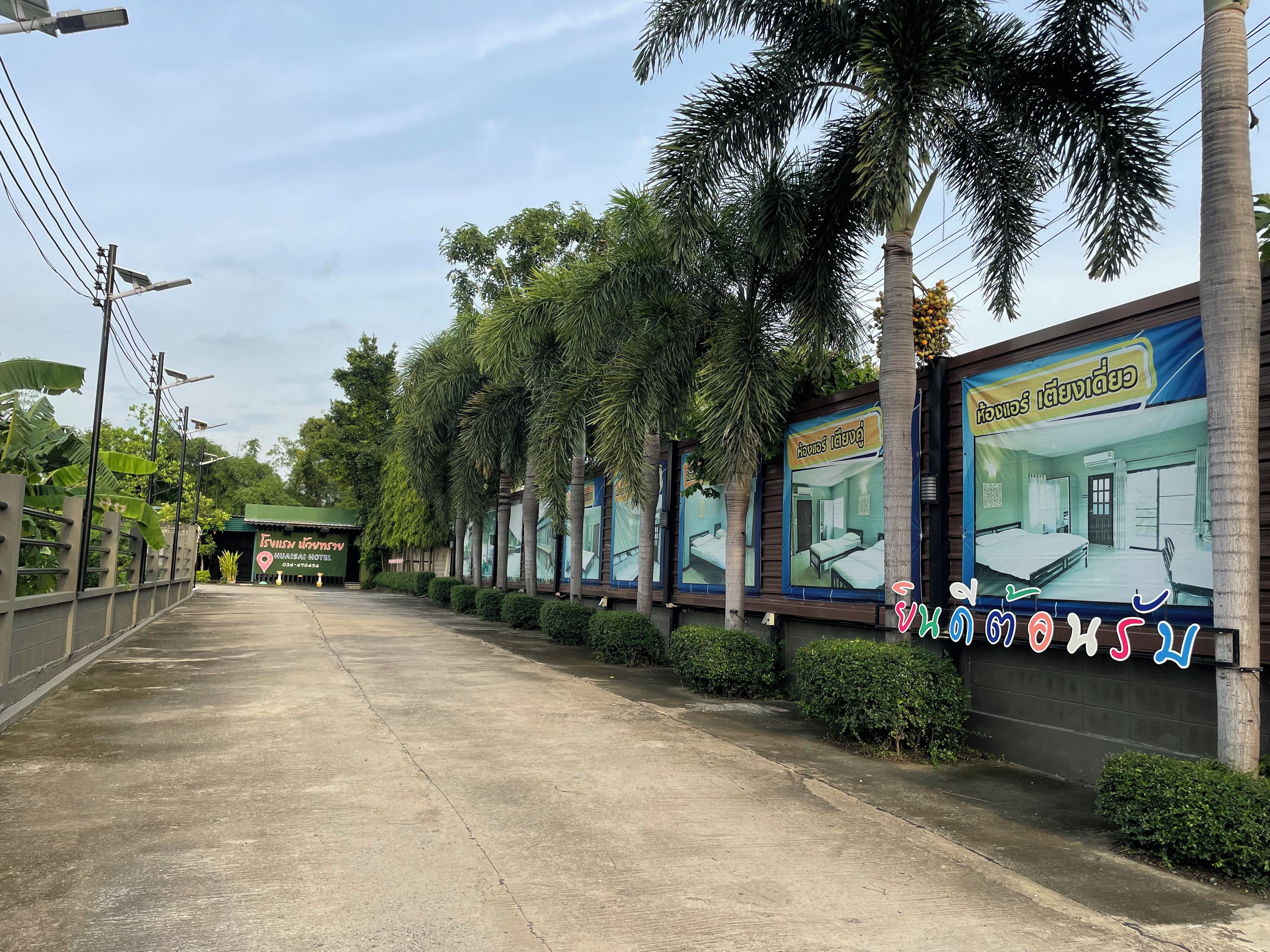 A pathway leading to a hotel with palm trees and a signboard.