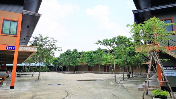 A courtyard with two buildings, one with a blue sign, trees, and a wooden ladder. - Huaisai Hotel (Nong Khae)
