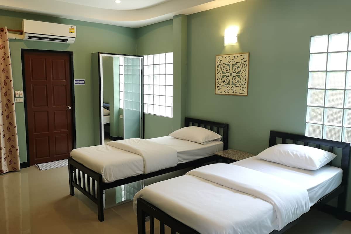 A room with two single beds, a mirror, a wall-mounted light, and a window with a decorative panel.