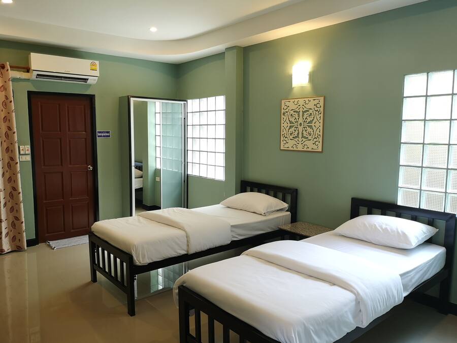 A room with two single beds, a mirror, a wall-mounted light, and a window with a decorative panel.