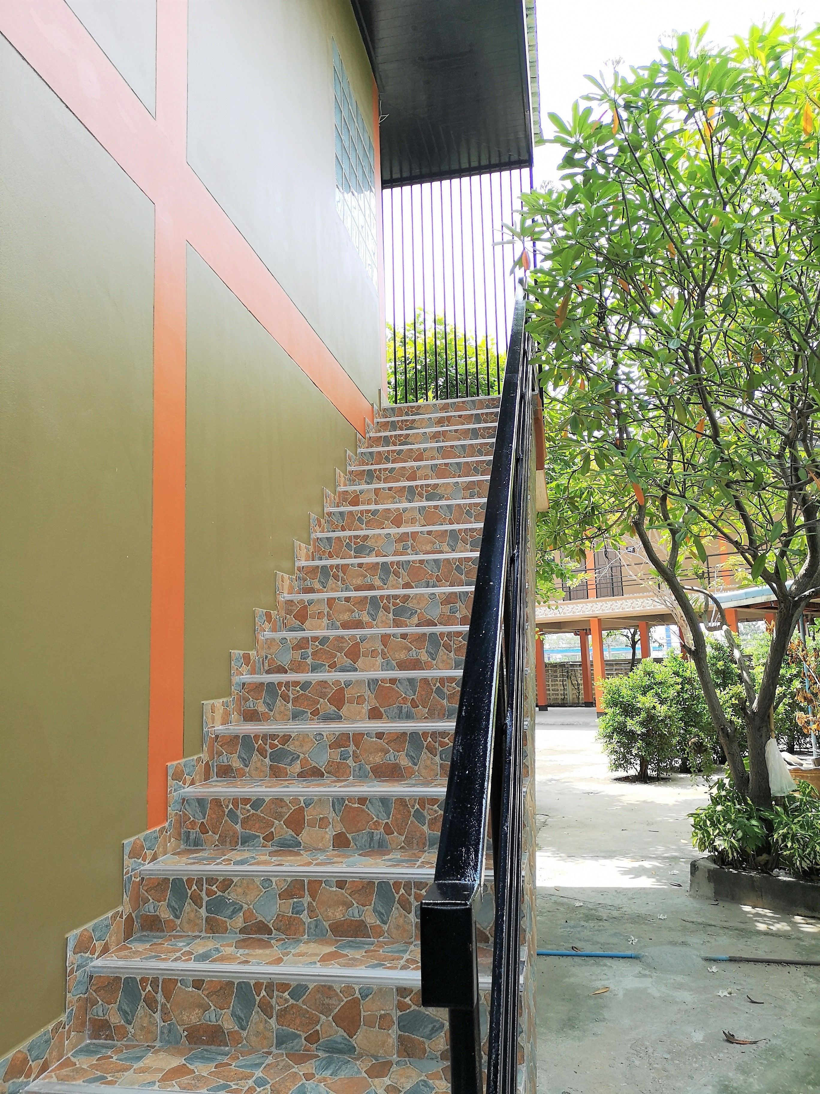 Una escalera de piedra con barandilla negra, que conduce a un edificio con fachada verde y naranja.