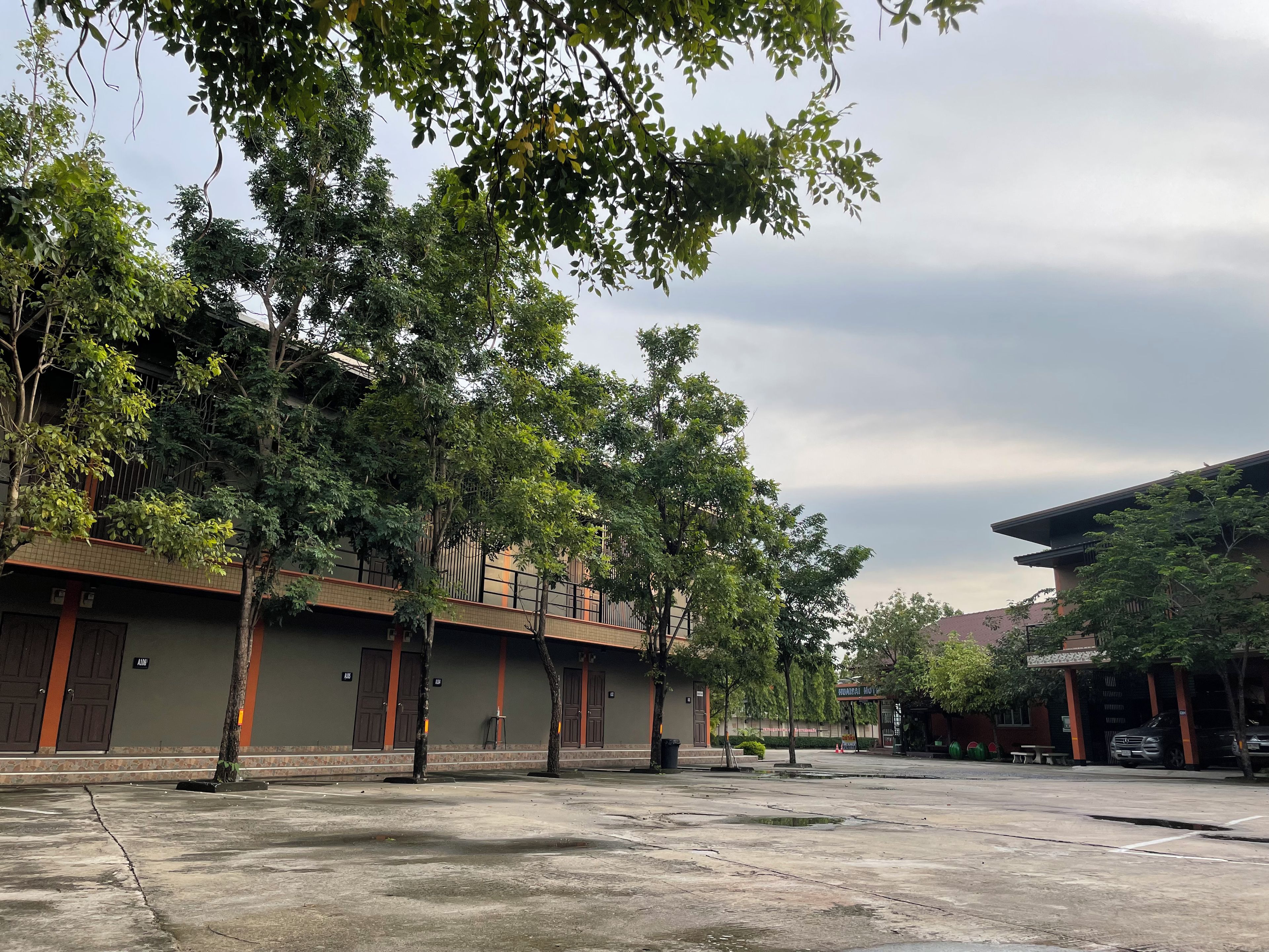 A courtyard with trees, a building with multiple doors, and a parking area.