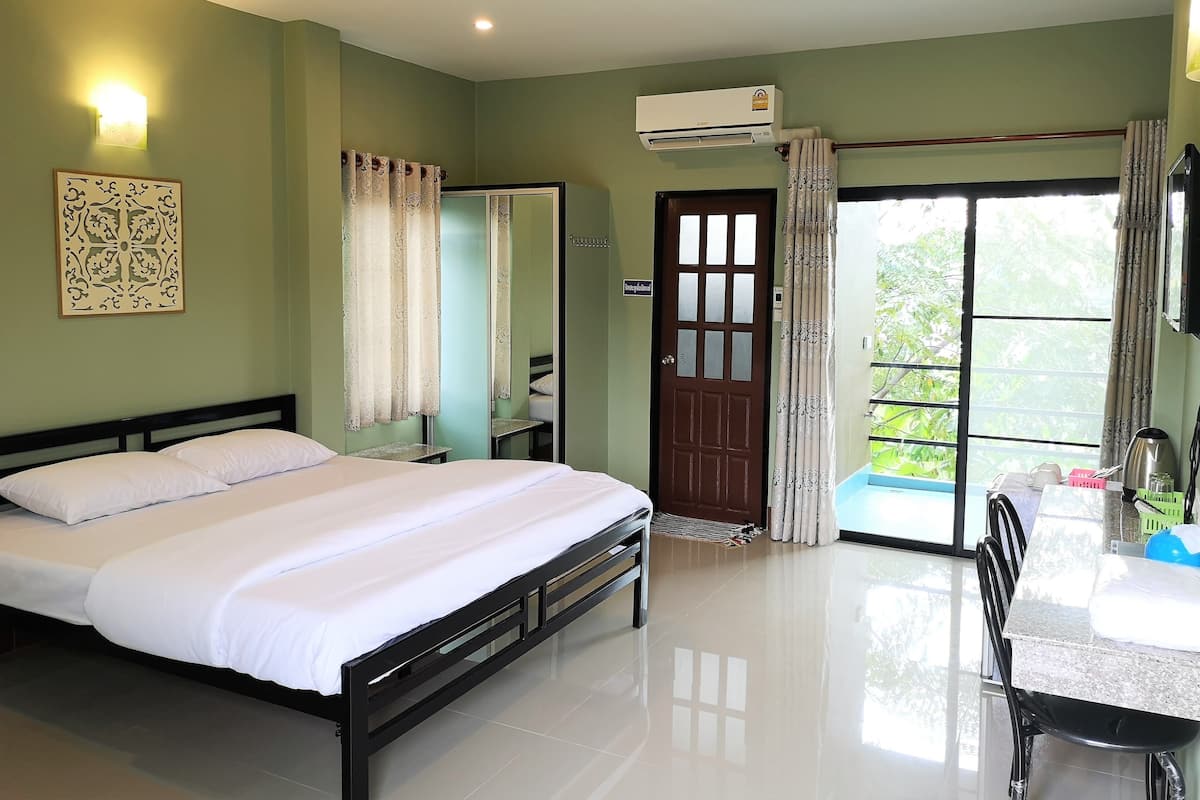 A hotel room with a bed, a desk, a chair, an air conditioning unit, and a view of the outdoors.