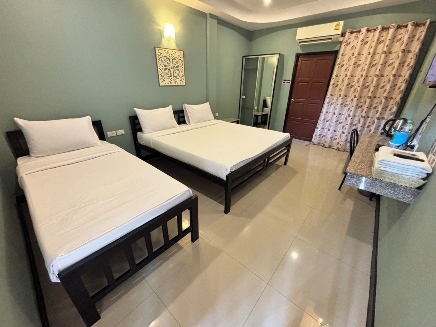 A hotel room with two single beds, a desk with a chair, a wardrobe, and a bathroom door.