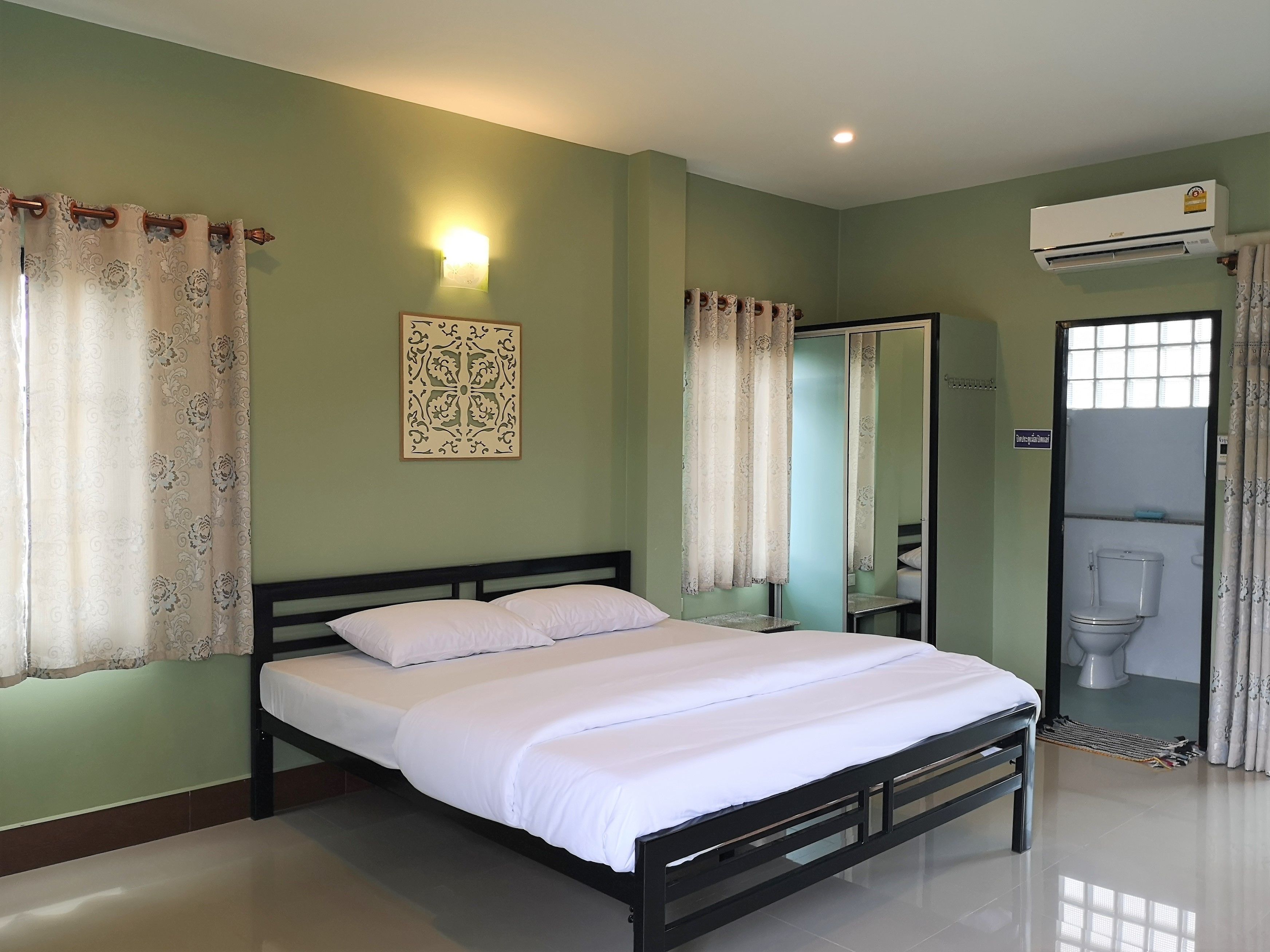 A bedroom with a bed, a wall-mounted air conditioner, a mirror, and a toilet visible through an open door.