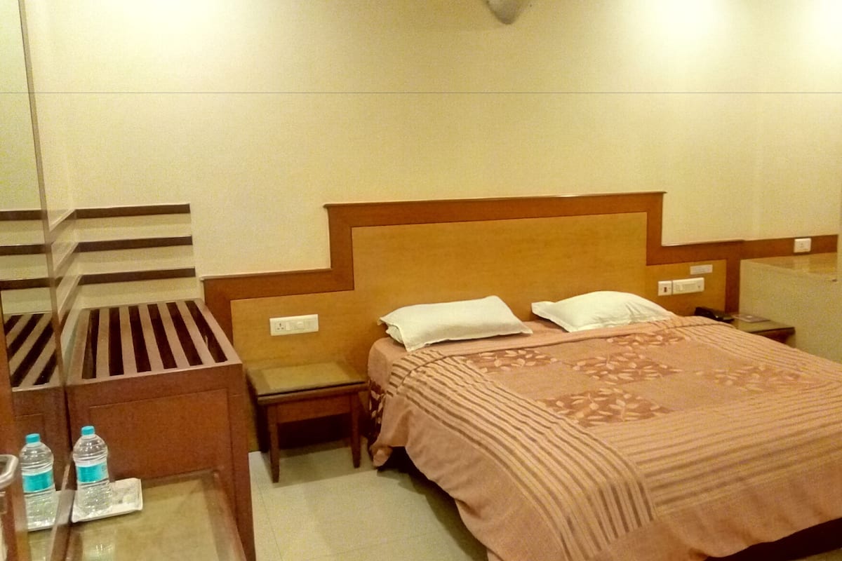 A hotel room with a bed, a nightstand, a chair, a desk with a lamp, and a water bottle on the floor.
