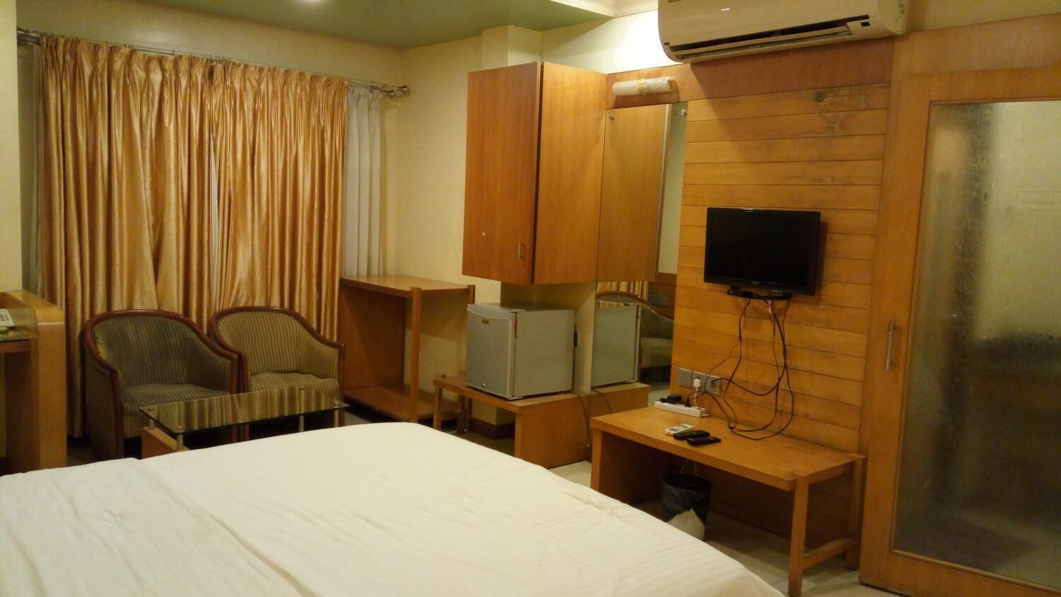 Habitación de hotel con una cama, dos sillones, un armario de madera, un escritorio pequeño con televisor y un espejo.