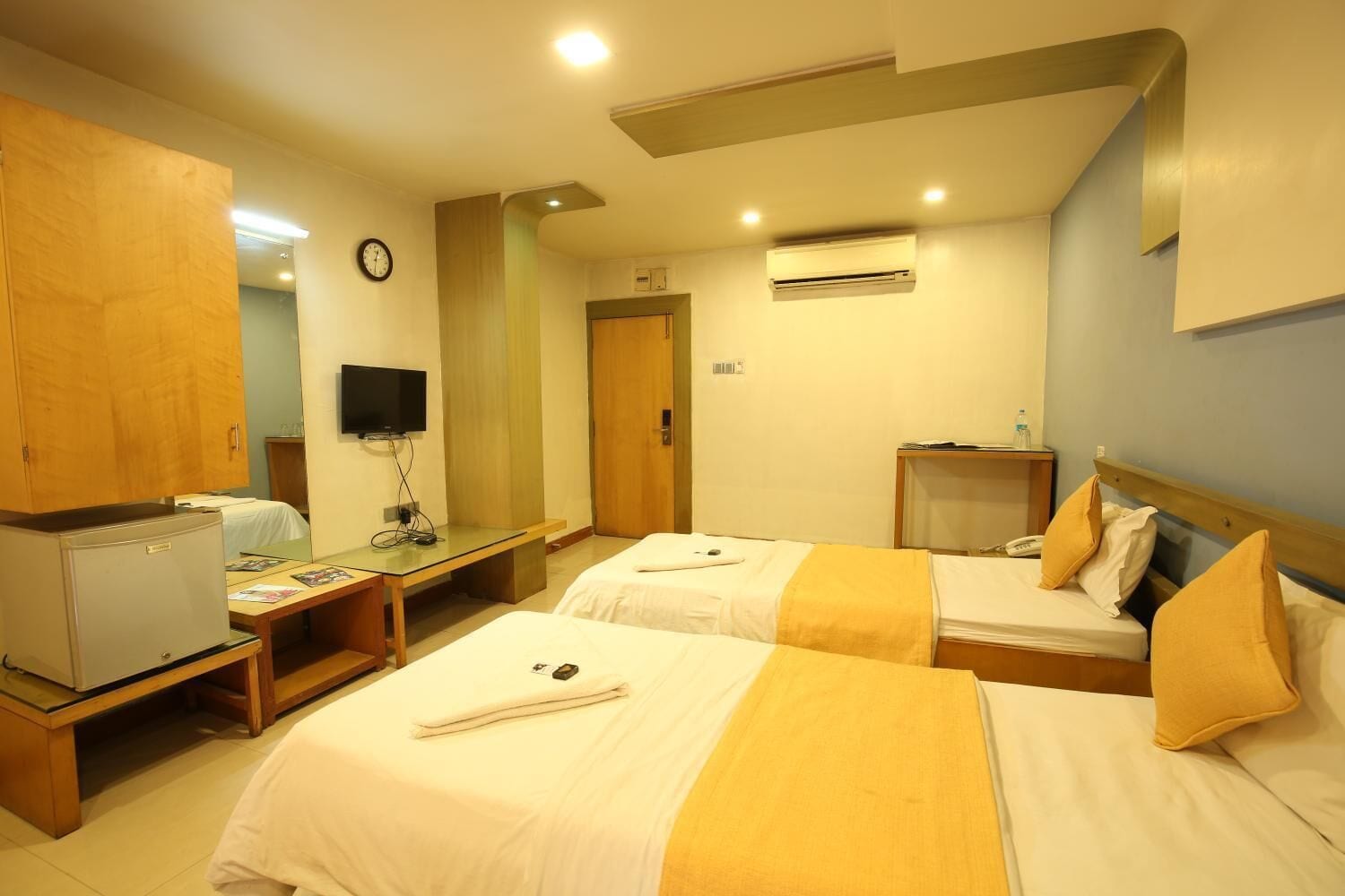 A hotel room with two beds, a desk, a television, and an air conditioning unit.