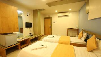 A hotel room with two beds, a desk, a television, and an air conditioning unit.