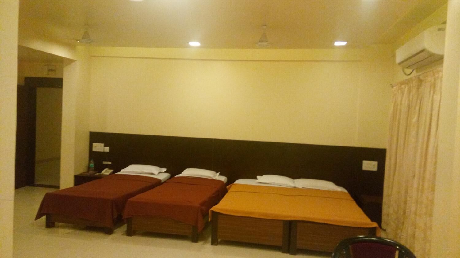 Une chambre d’hôtel avec deux lits simples et un lit plus grand, tous dotés de têtes de lit et de tables de chevet.
