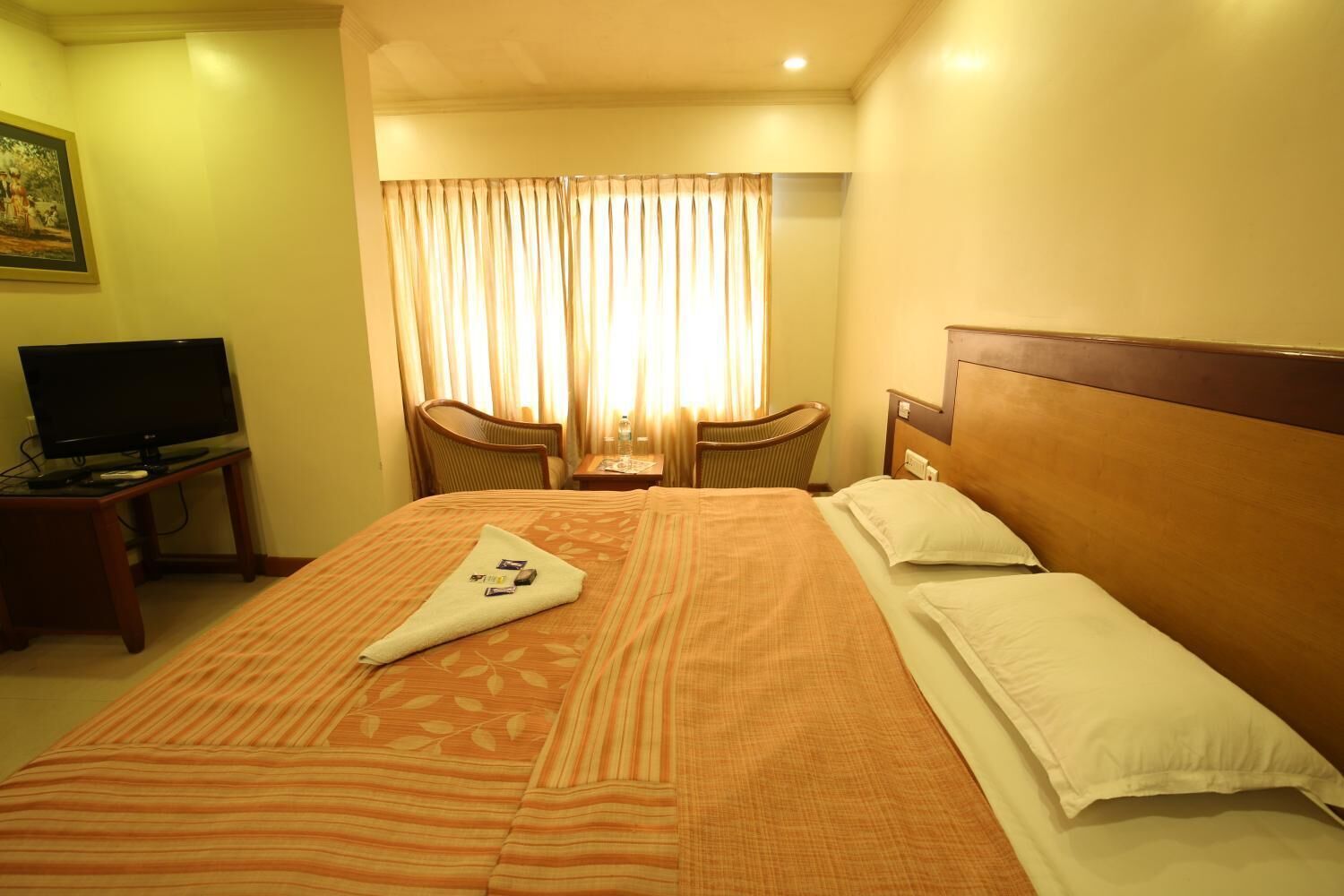 A hotel room with a large bed, a television on a side table, and a window with curtains.