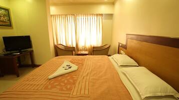 A hotel room with a large bed, a television on a side table, and a window with curtains.