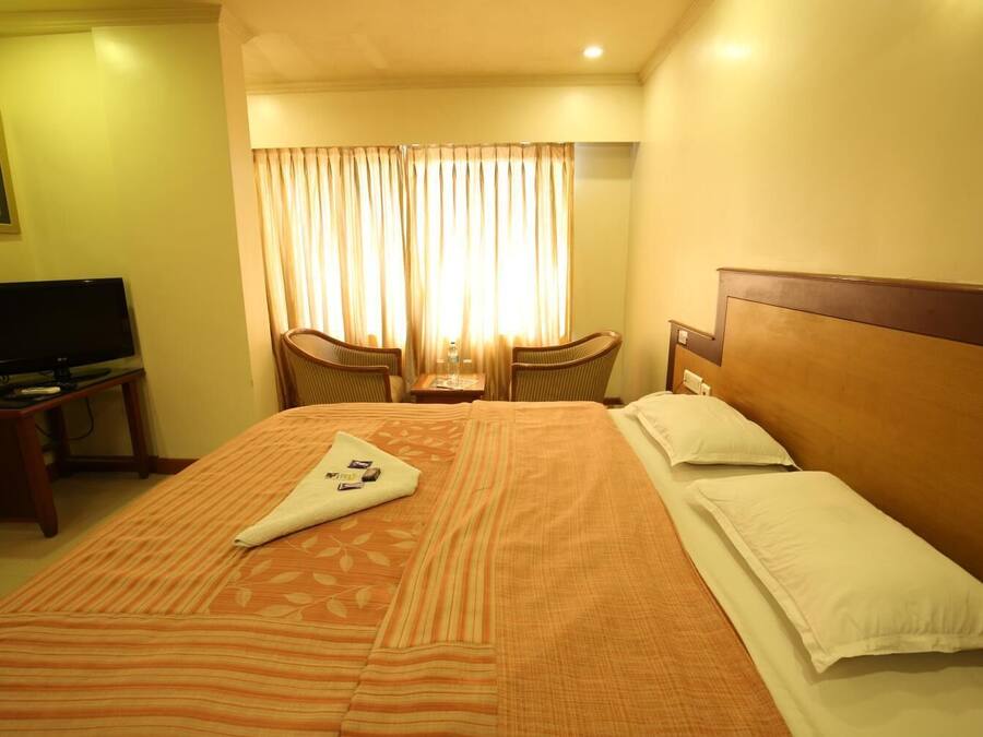 A hotel room with a large bed, a television on a side table, and a window with curtains.