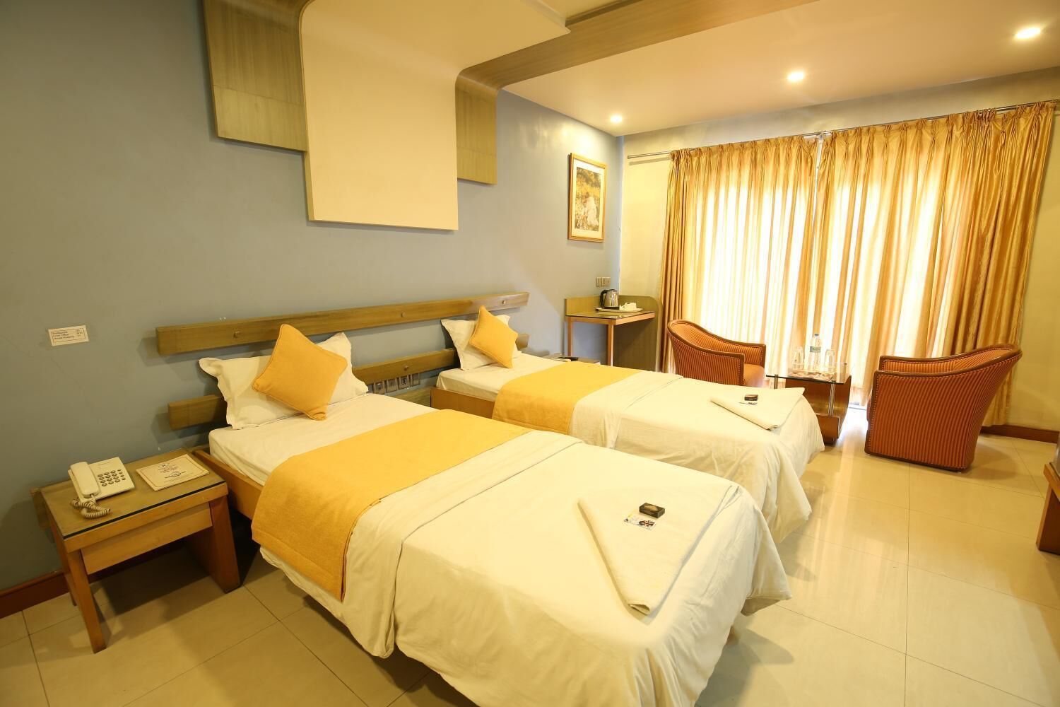 A hotel room with two beds, a desk, a chair, and a window with curtains.