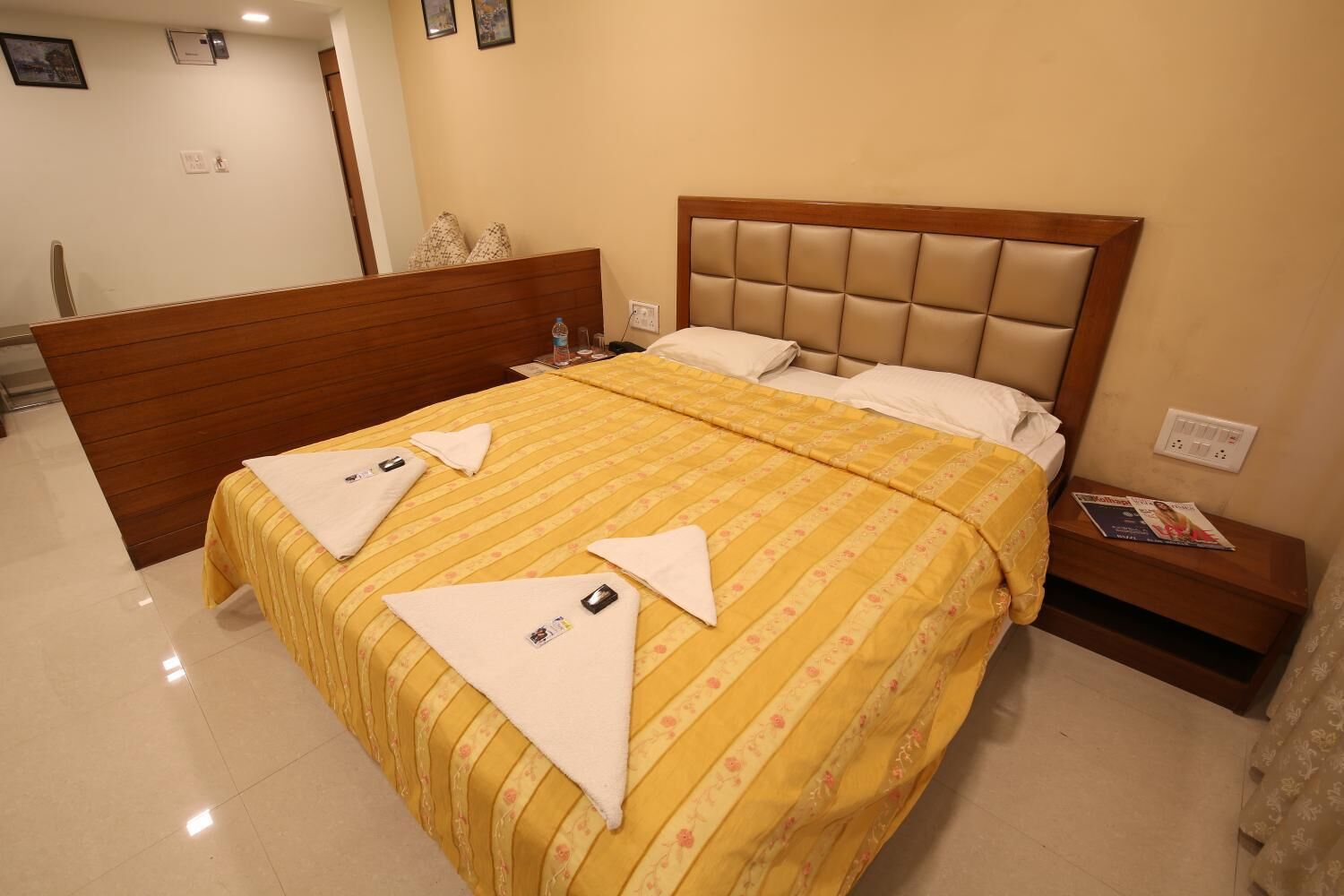 A hotel room with a bed, wooden headboard, and a nightstand with a magazine.